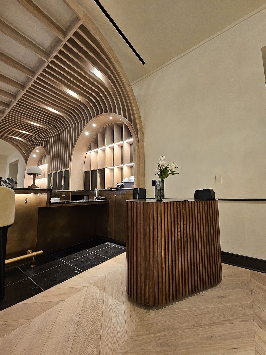 Reception podium — ribbed walnut with brass back bar beyond